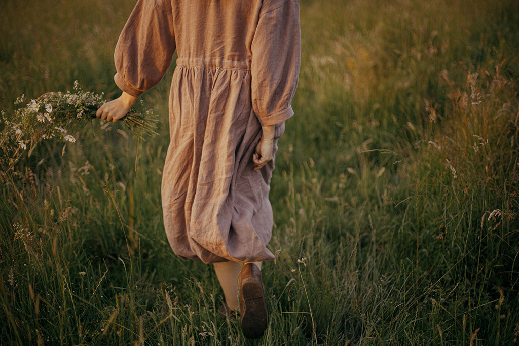 Woman wearing a natural European linen dress with soft wrinkles, walking outdoors in the fields