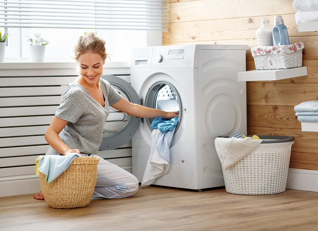 Woman loading laundry into washing machine at home, holding a basket of clothes