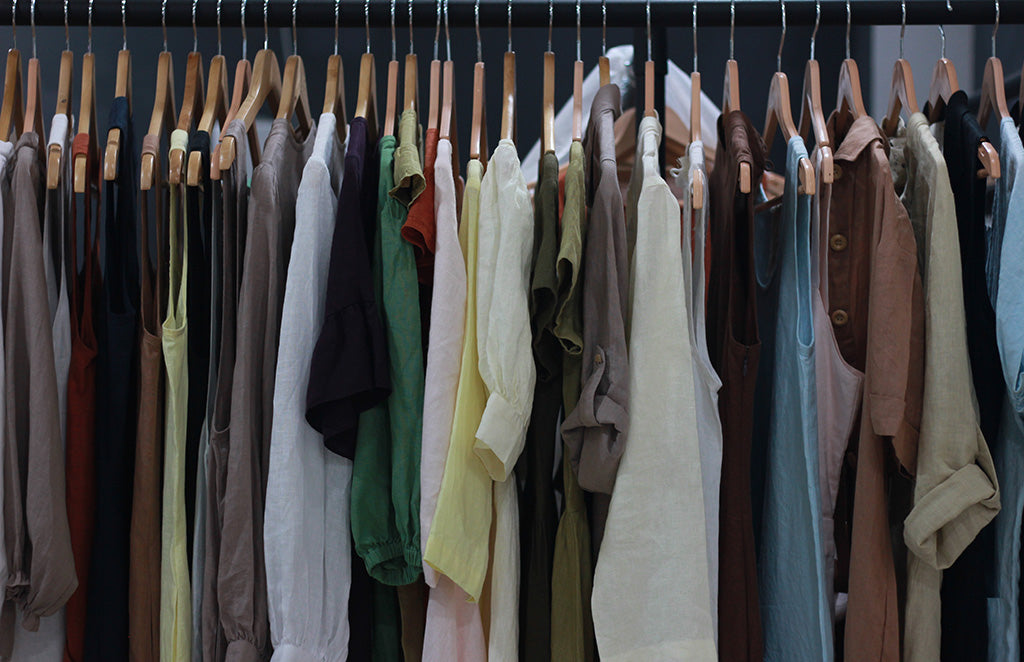 Assorted linen dresses and shirts in earthy tones hanging neatly on wooden hangers