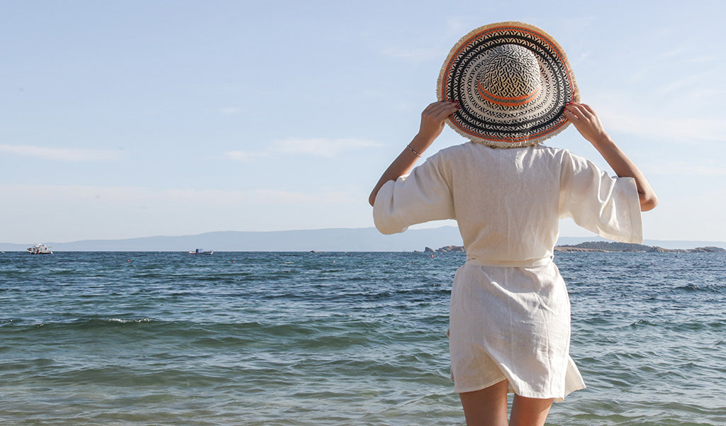 Woman standing on the beach in a linen dress and a straw hat