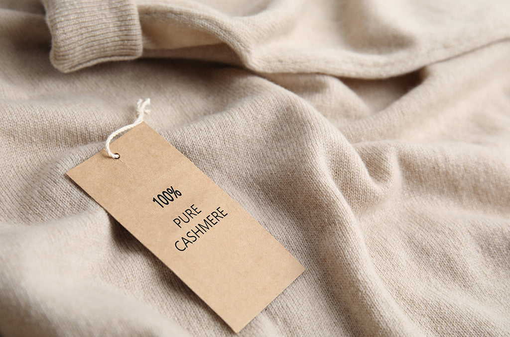 Close-up of soft beige cashmere sweater fabric with a tag labeled 100% pure cashmere