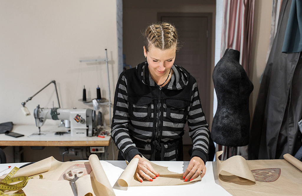 Fashion designer working on a clothing pattern at a studio table with sewing tools