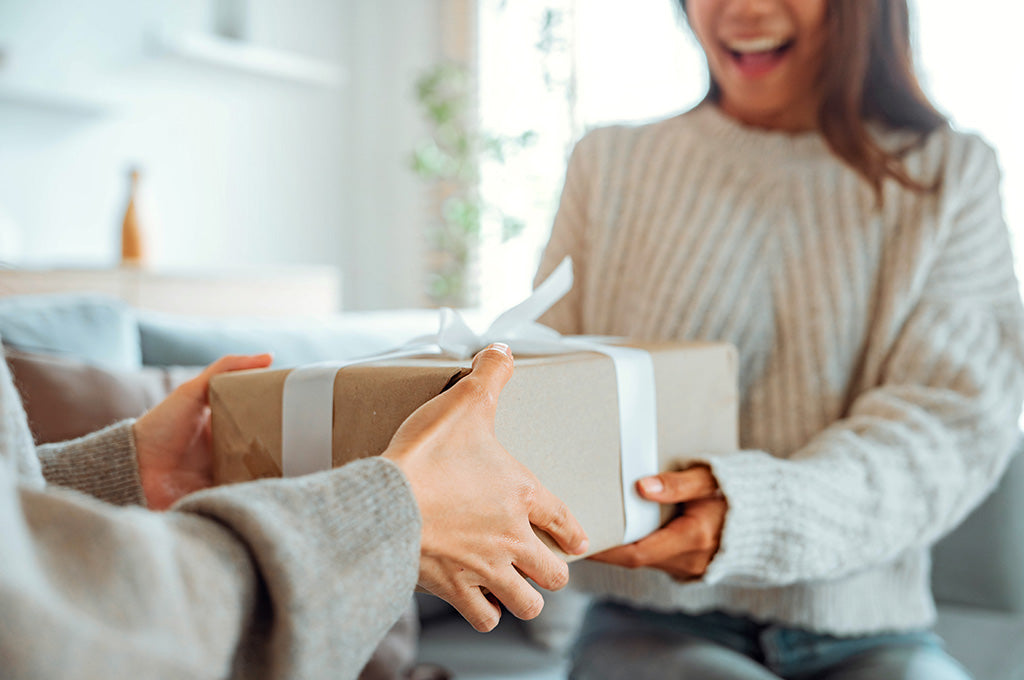 Woman smiling while receiving a wrapped gift in a cozy home setting