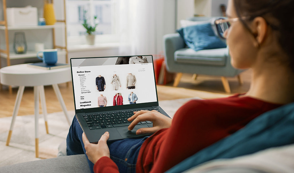 Woman sitting at home reviewing clothing options on a laptop