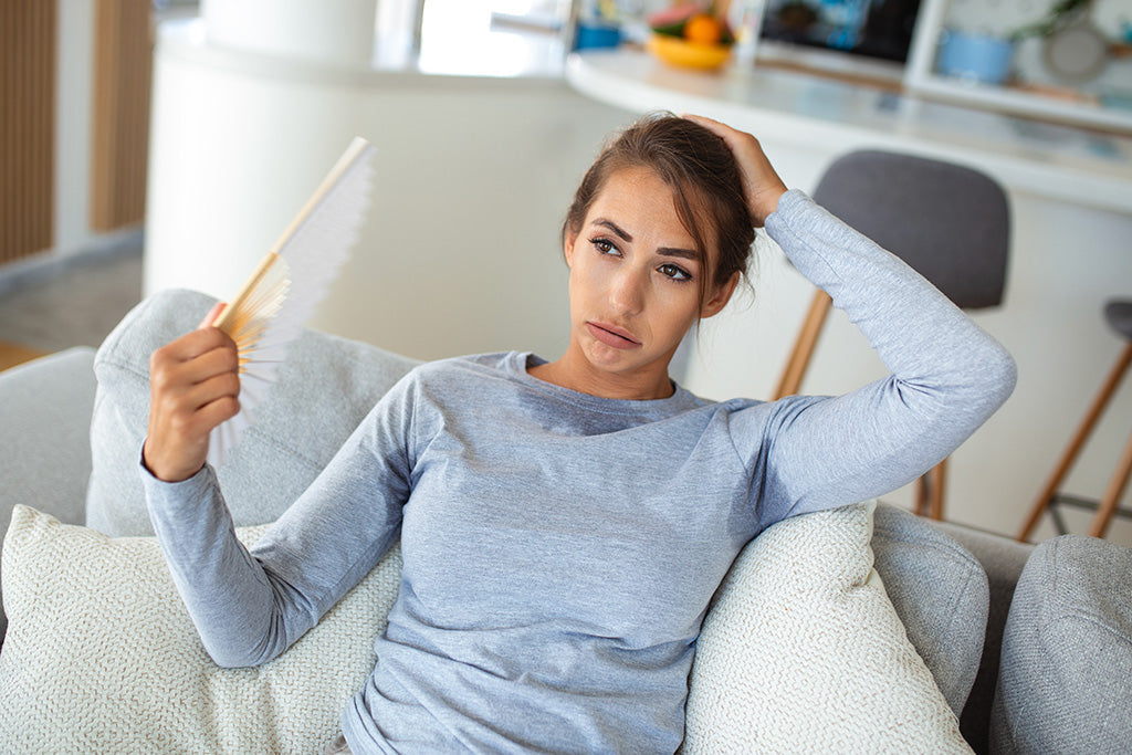 Woman feeling overheated in non-breathable clothing while sitting indoors during warm weather