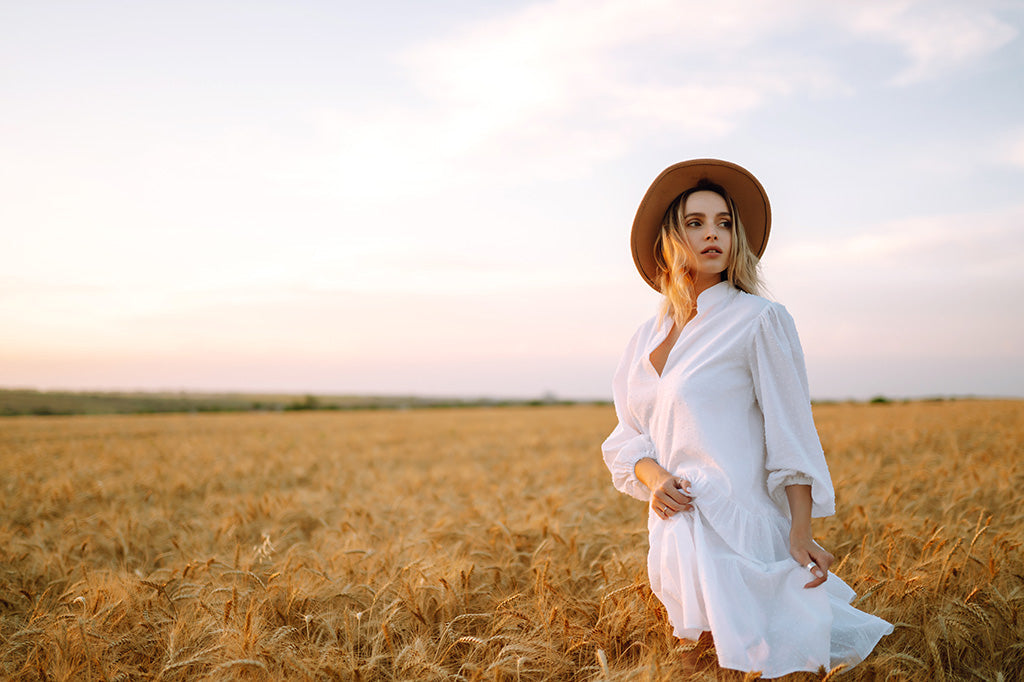 Woman in a white dress and hat standing in warm natural sunlight