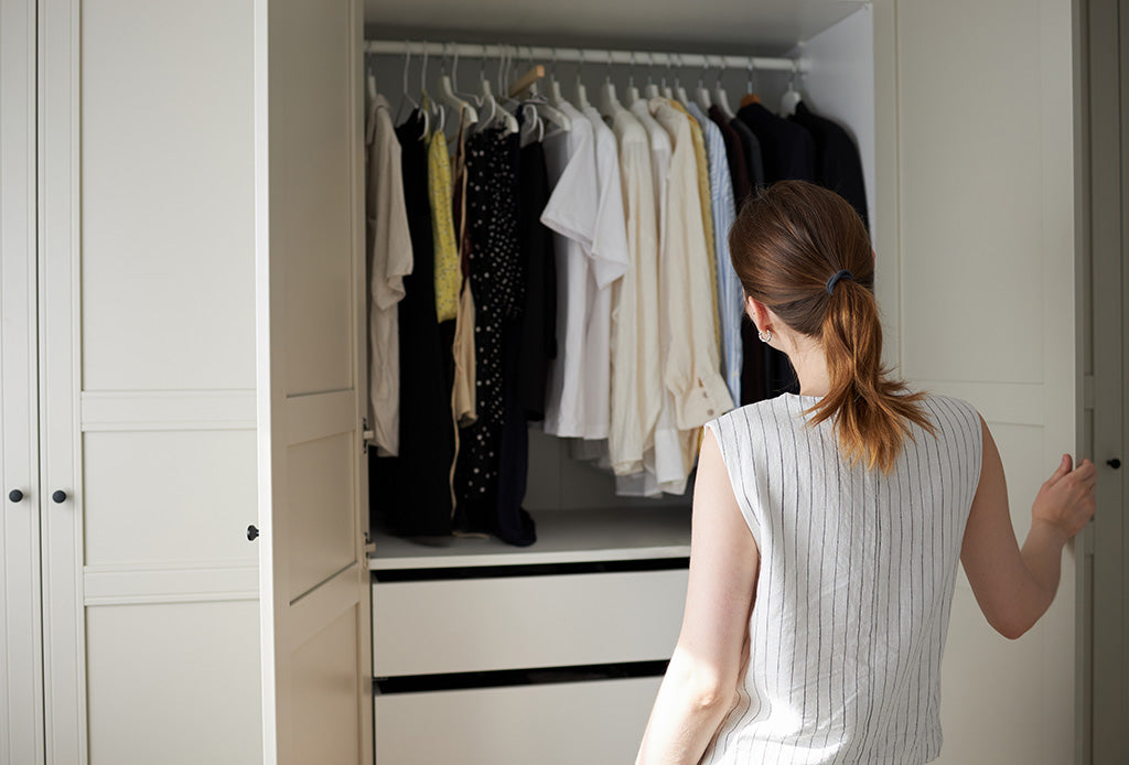 A woman standing in front of an open wardrobe filled with neatly hanging clothes, choosing what to wear