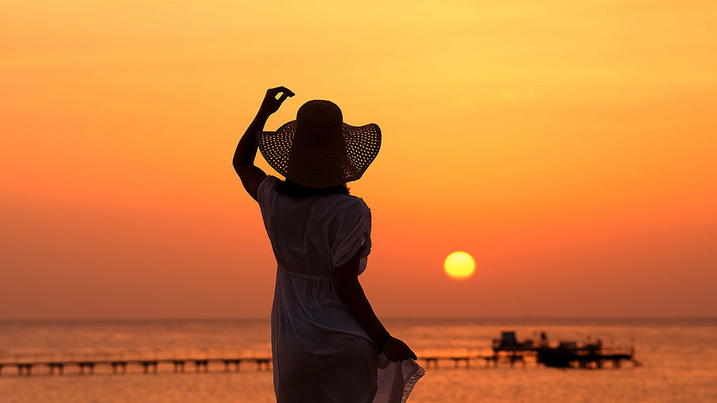 Woman in a flowing summer dress and wide-brim hat watching the sunset