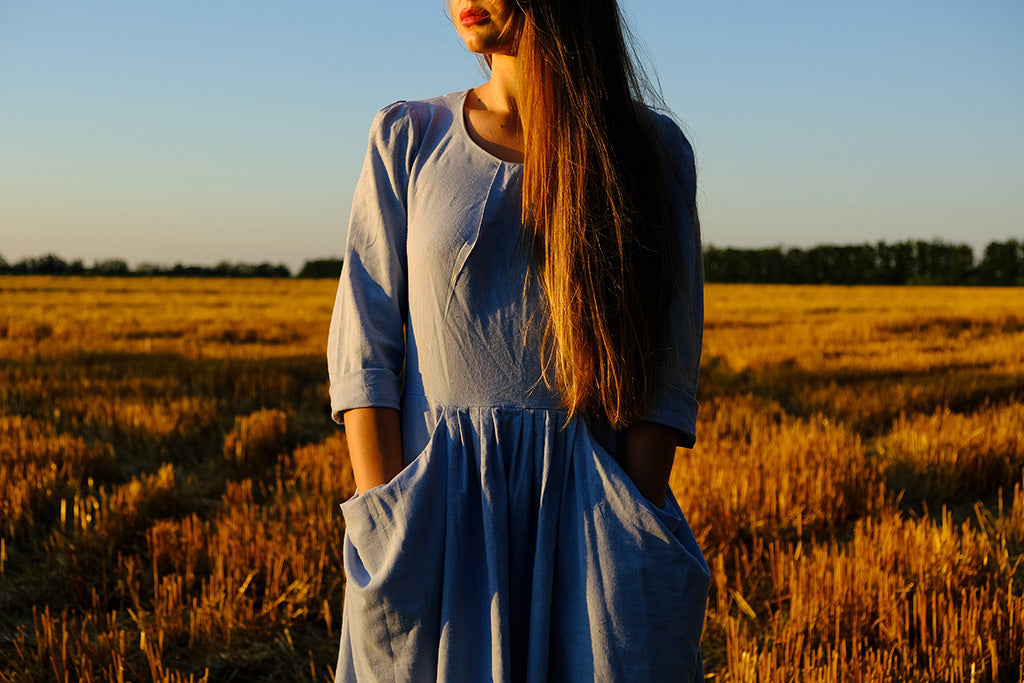 Woman wearing a relaxed linen dress with pockets while standing in a golden field at sunset