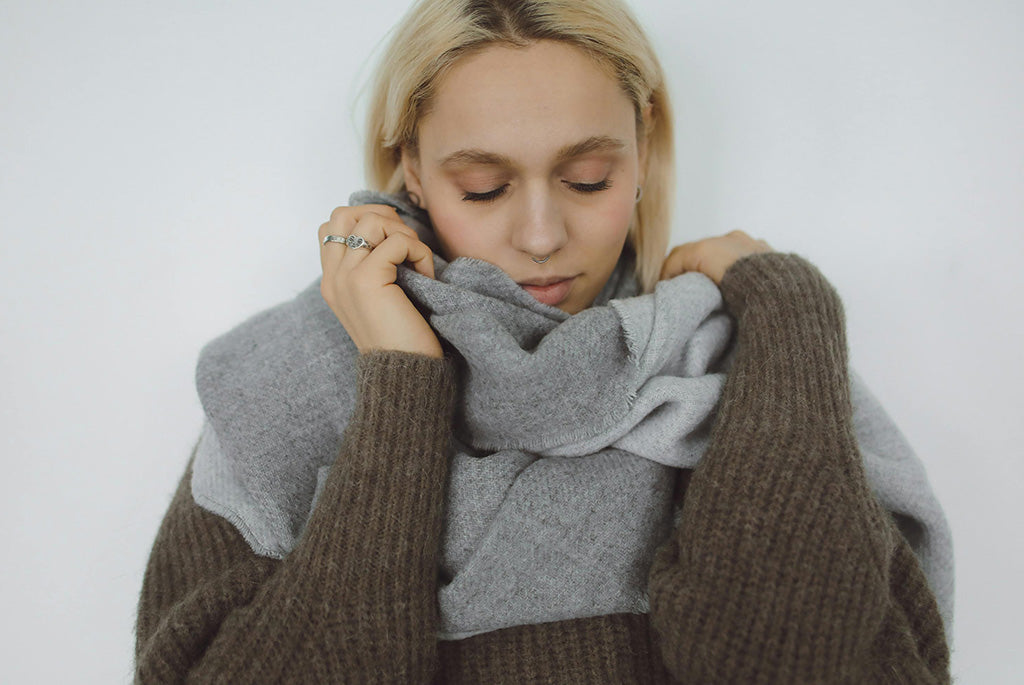 Close-up of a woman wrapped in a soft grey wool scarf and knit sweater