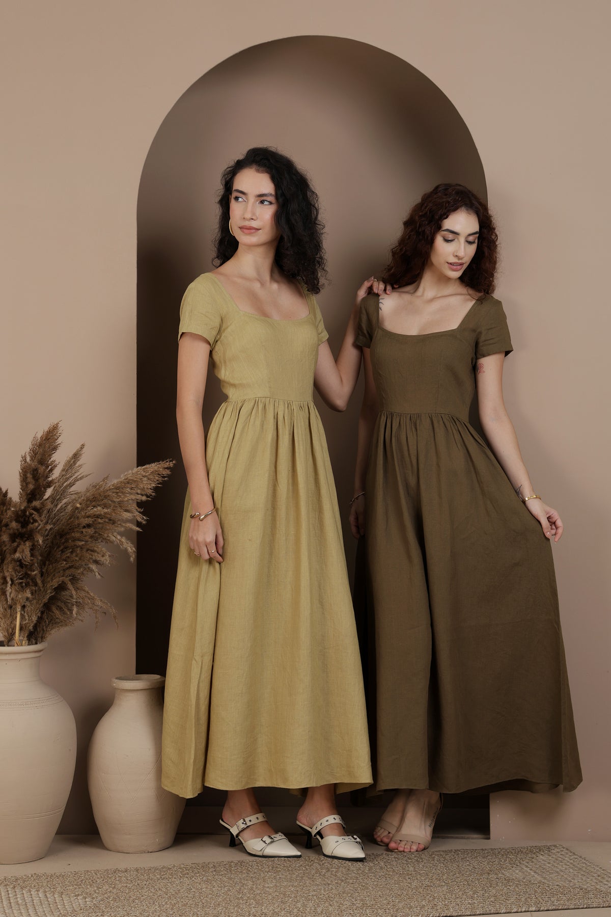 Two women wearing long dresses standing in front of an archway