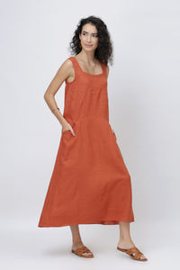 woman modeling a sleeveless rust-red linen midi dress with side pockets