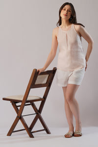 Woman in a sleeveless linen top and shorts standing next to a wooden chair 