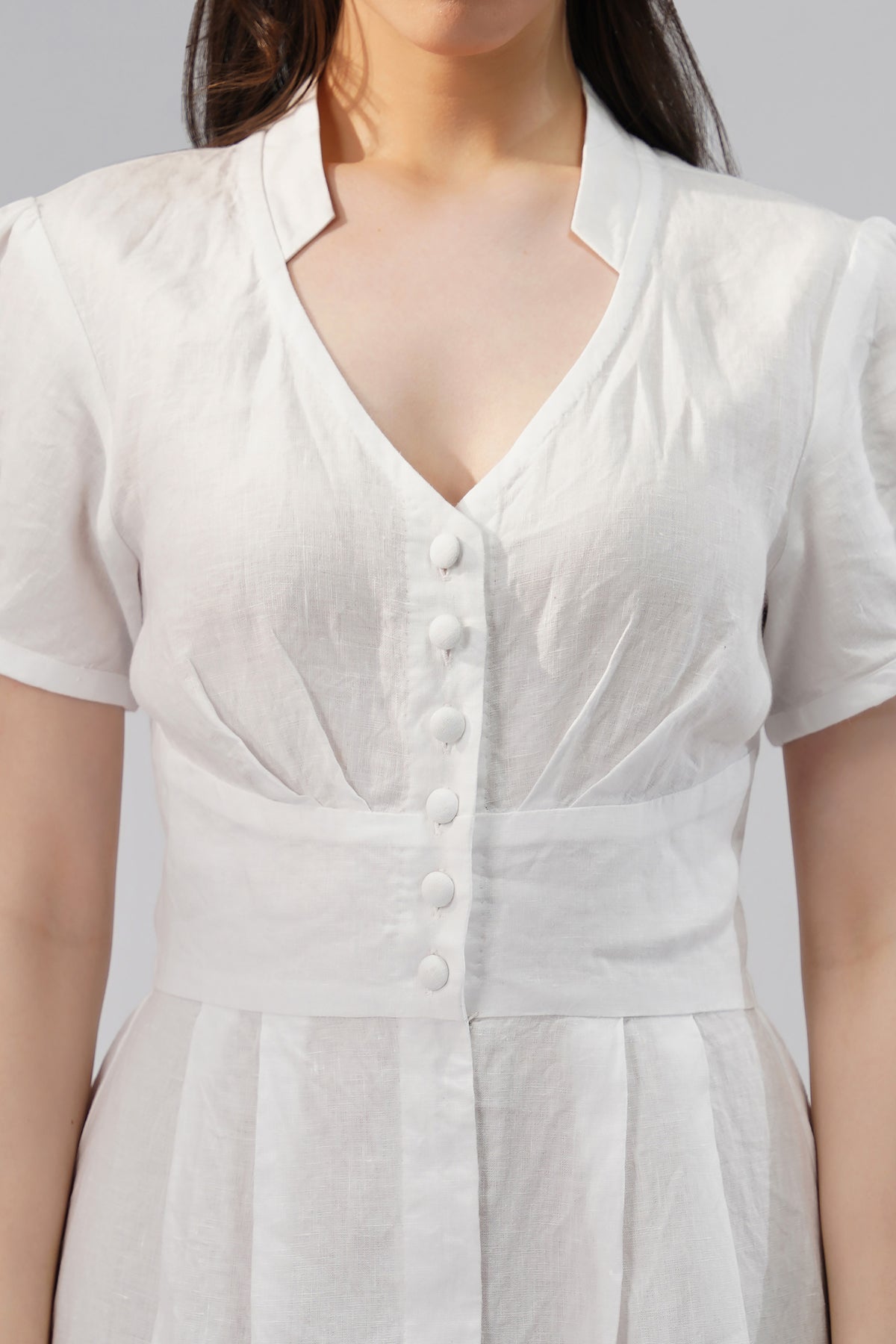 Close-up of European linen dress featuring V-neckline, front button placket, puff sleeves and structured waist