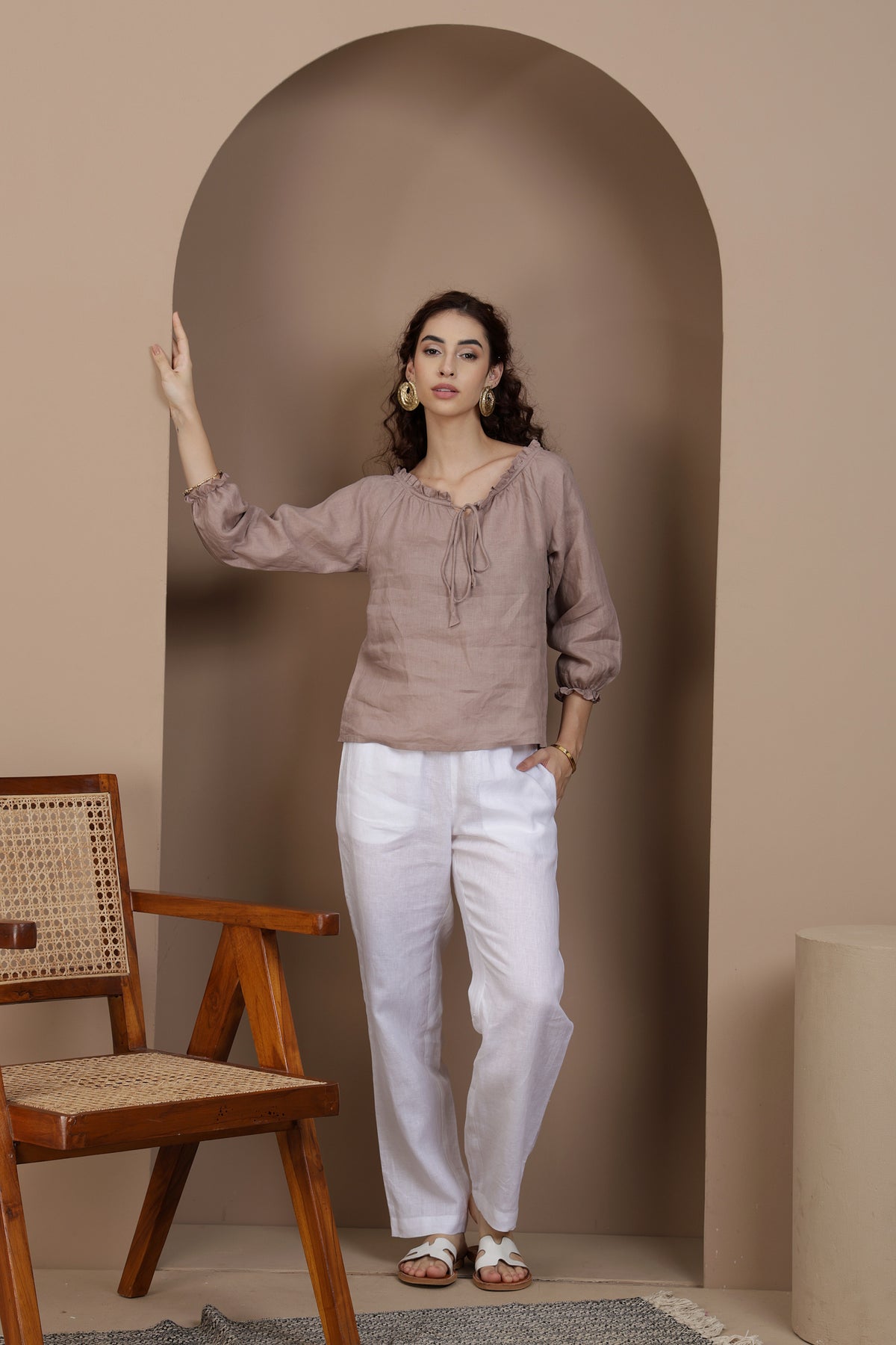 Woman wearing linen top standing in a room with a wooden chair and archway.