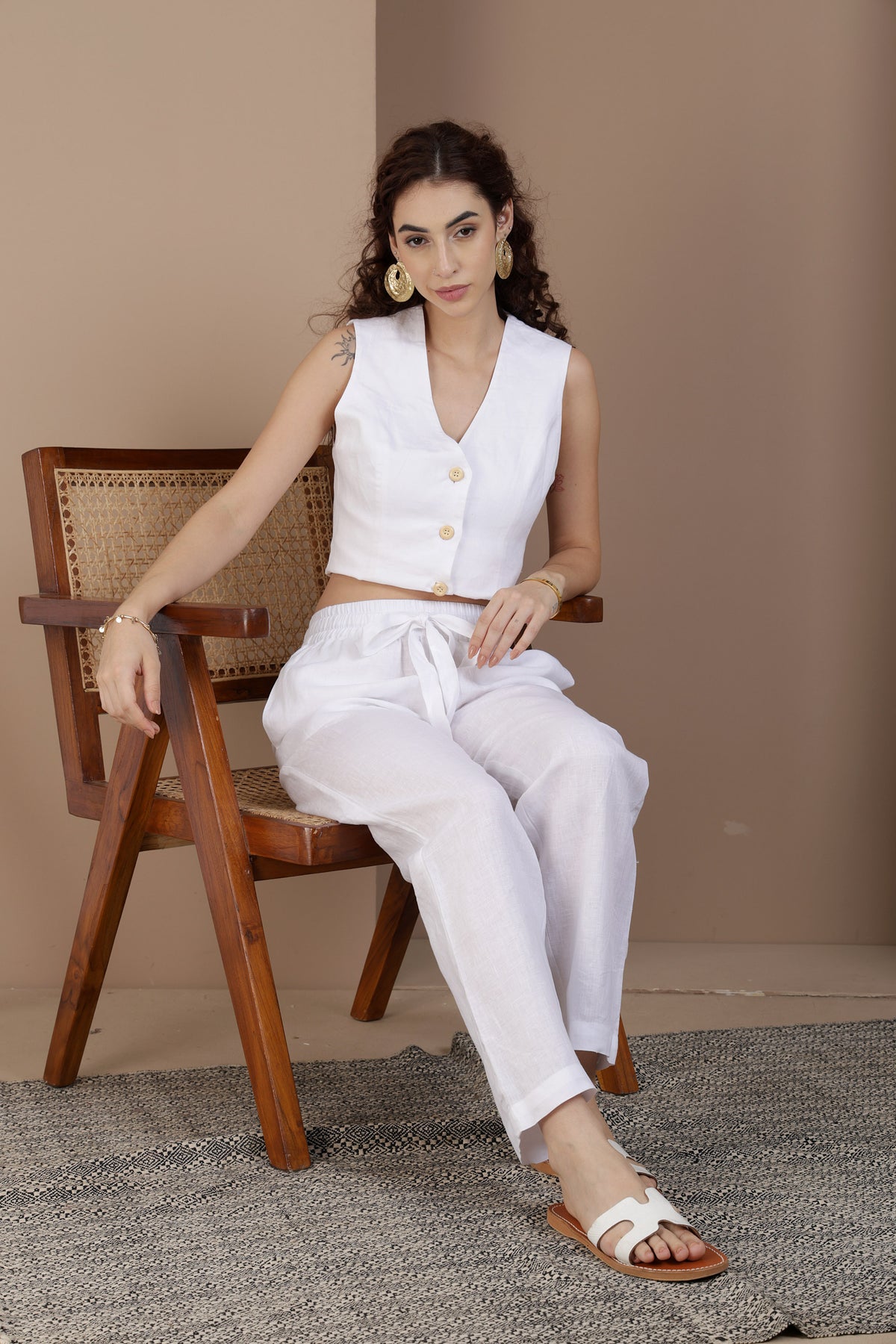 Woman wearing white linen relaxed pant sitting on a wooden chair