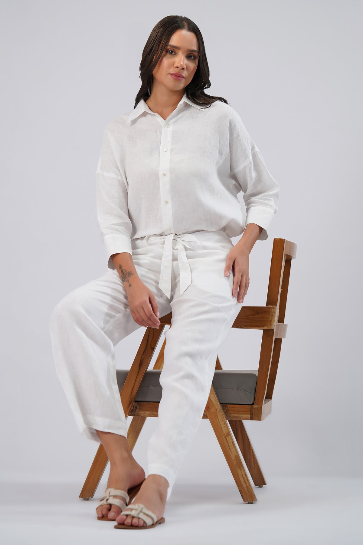 Woman in a white linen outfit sitting on a wooden chair 