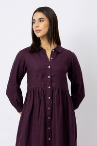 Woman wearing a linen dress with a rounded collar, button-front design, long sleeves, and gathered waist