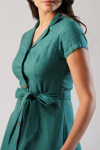 Close-up of a woman wearing a dark jade linen dress with a lapel collar, short sleeves, button front, and tie waist