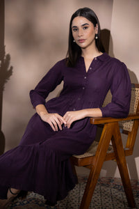 Woman wearing a velvet plum linen dress seated on a wooden chair