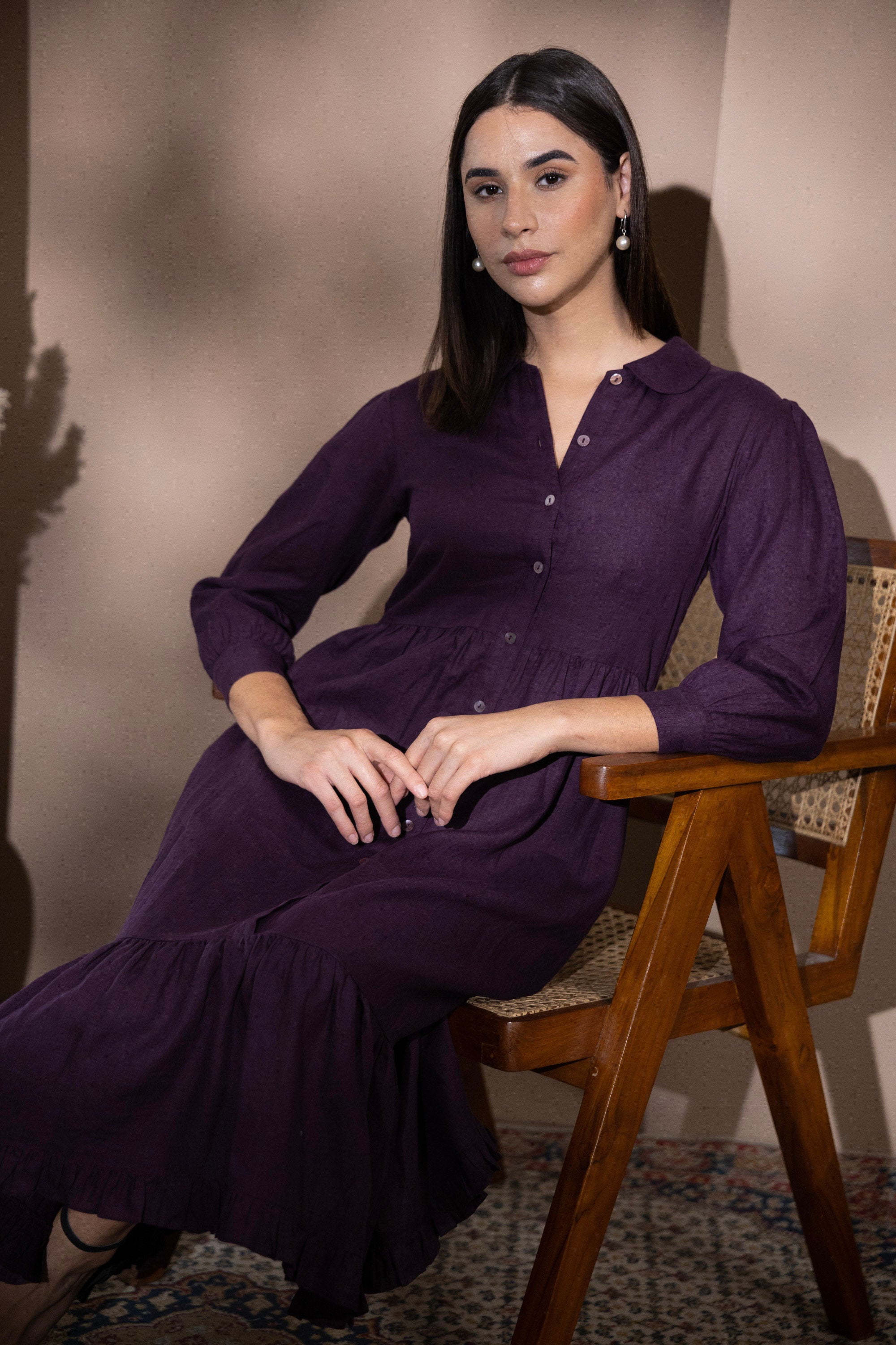 Woman wearing a velvet plum linen dress seated on a wooden chair
