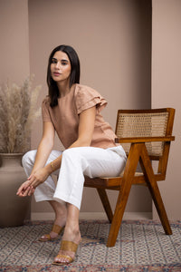 Woman wearing a linen flutter-sleeve top with white linen pants seated in a wooden armchair