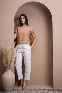 Woman wearing a linen flutter-sleeve top with white linen pants in a refined neutral interior