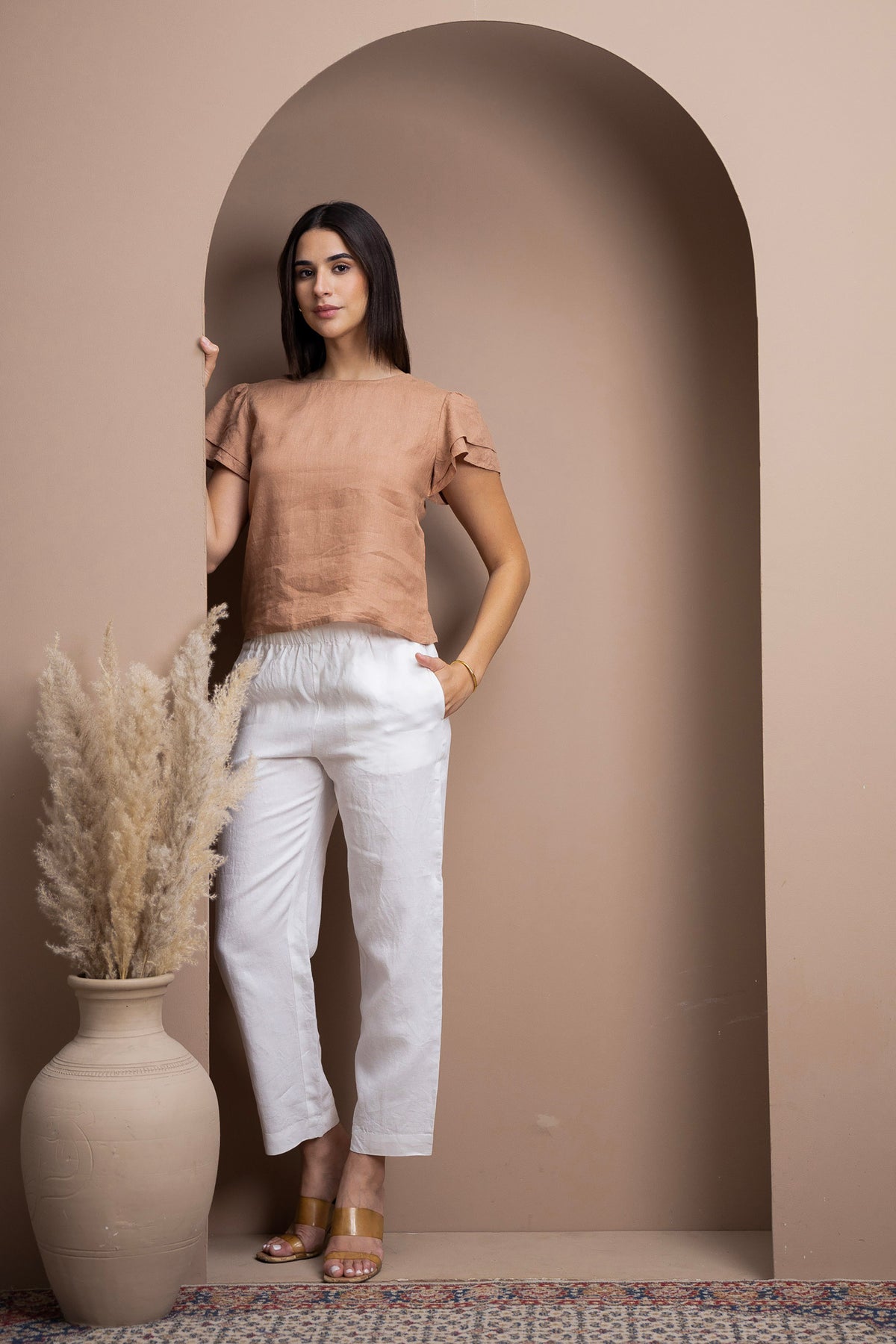 Woman wearing a linen flutter-sleeve top with white linen pants in a refined neutral interior