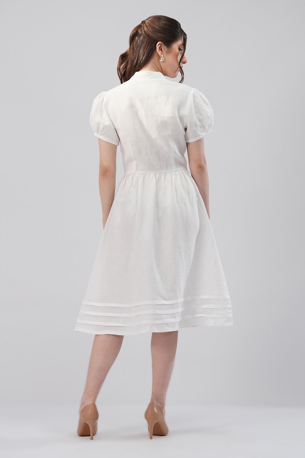 Back view of a linen midi dress with short puff sleeves, fitted waist and horizontal pintuck hem detailing