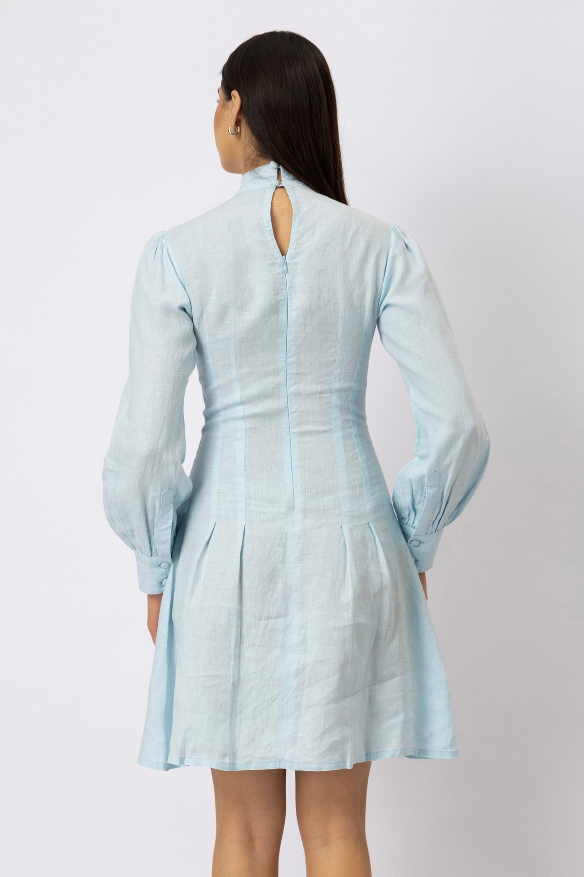 Back view of a tailored linen mini dress featuring a keyhole neckline, concealed zipper, bishop sleeves, and box pleats