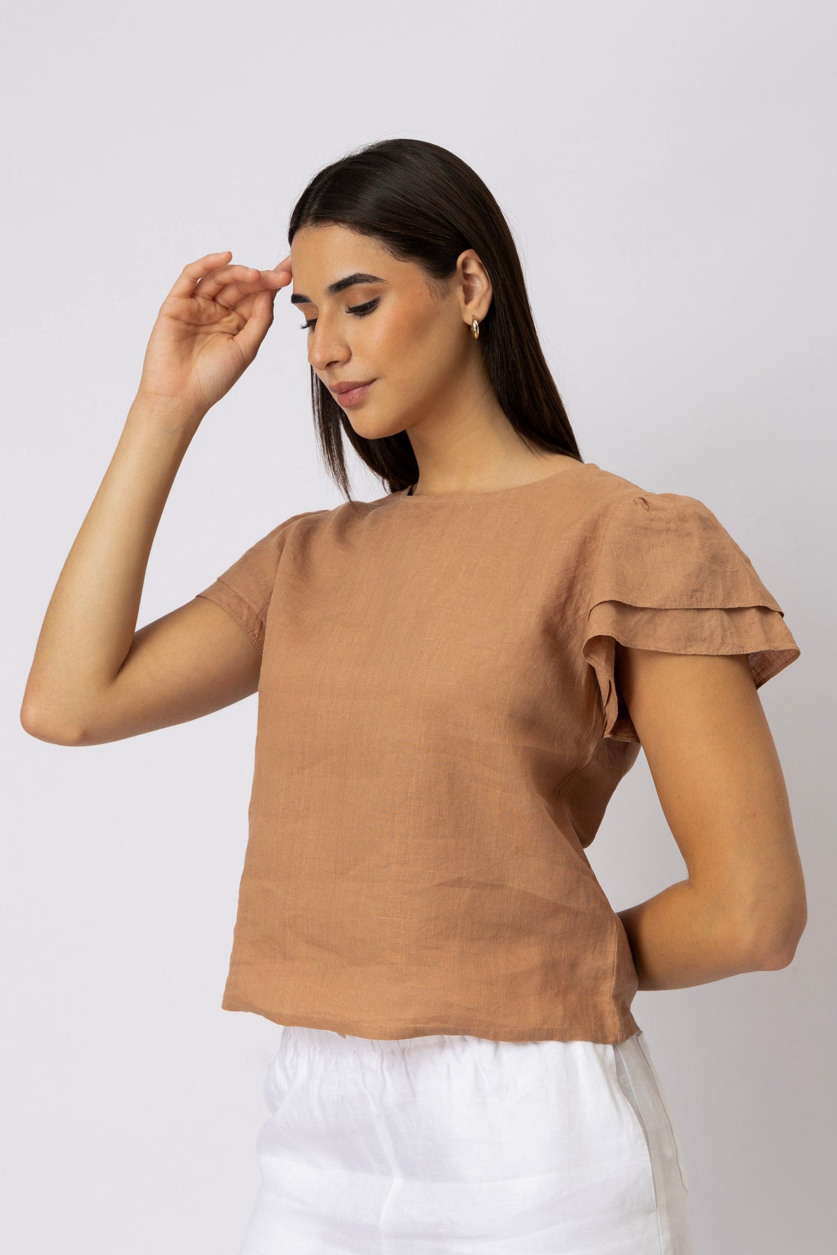 Side view of a woman wearing a linen top with layered flutter sleeves and a relaxed silhouette
