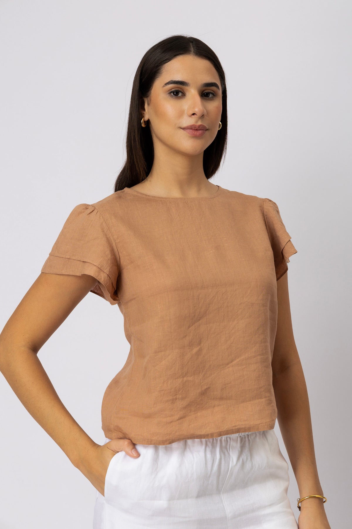 Three-quarter view of a woman wearing a linen top with layered flutter sleeves and a round neckline