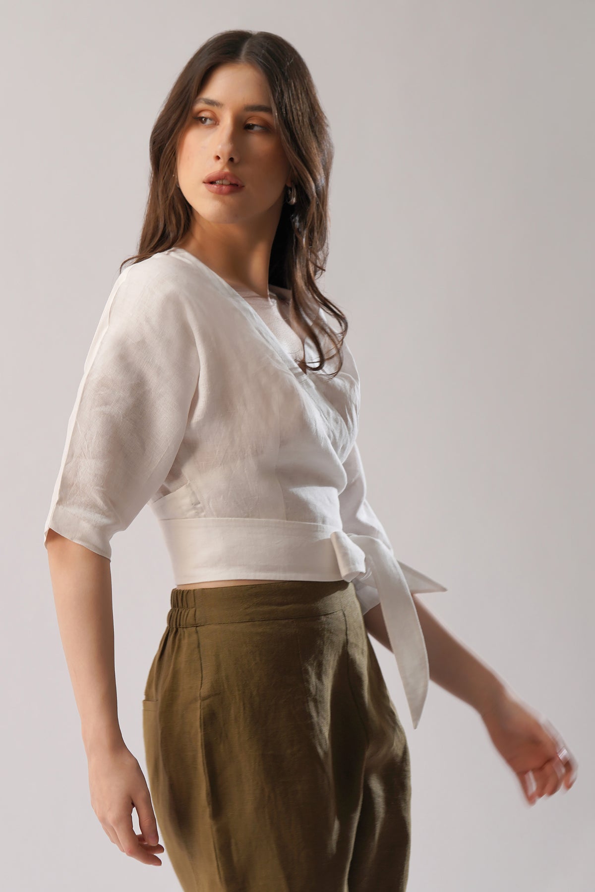 Woman wearing a white linen wrap top and brown linen pants 