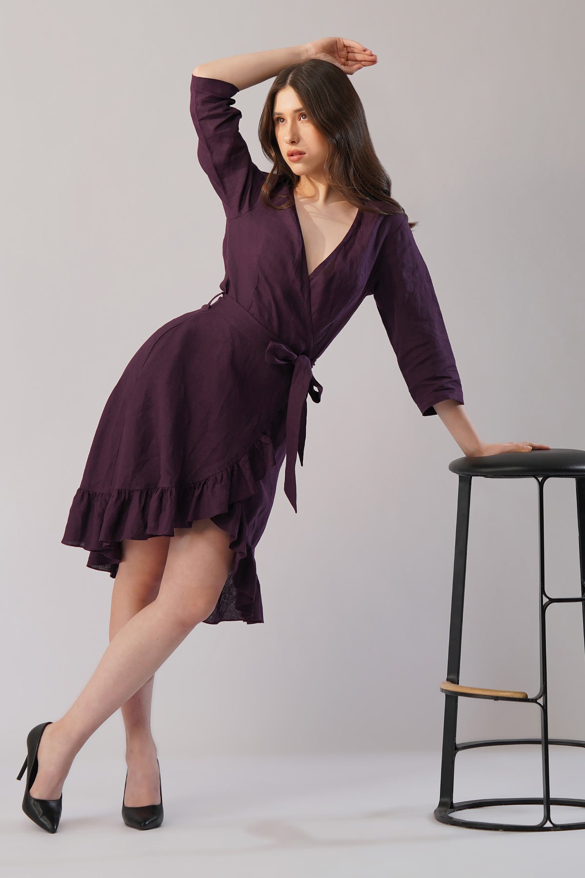 Woman in a purple dress posing next to a black stool