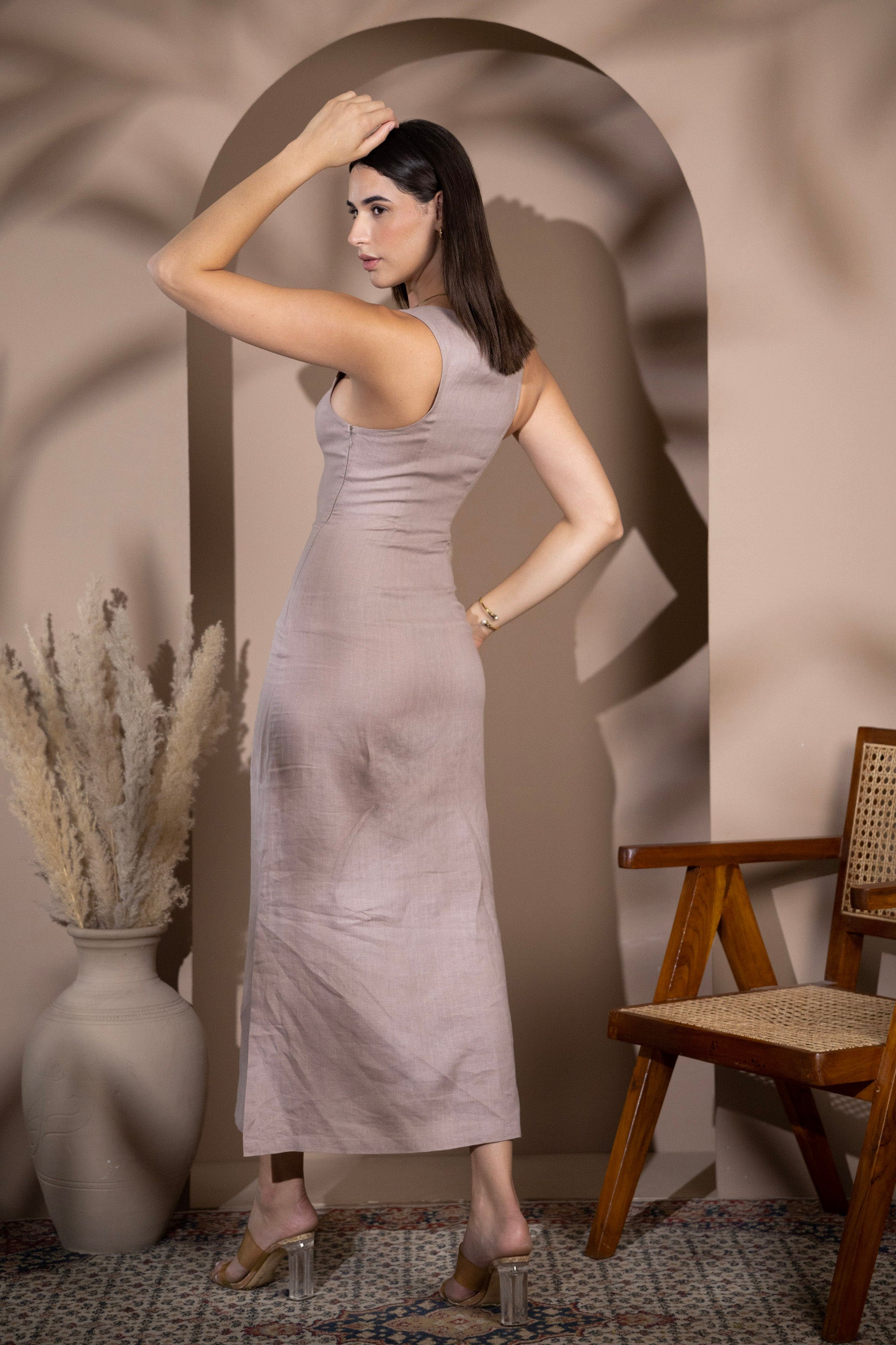 Woman wearing a linen fitted midi dress, shown from the back in a warm minimalist interio