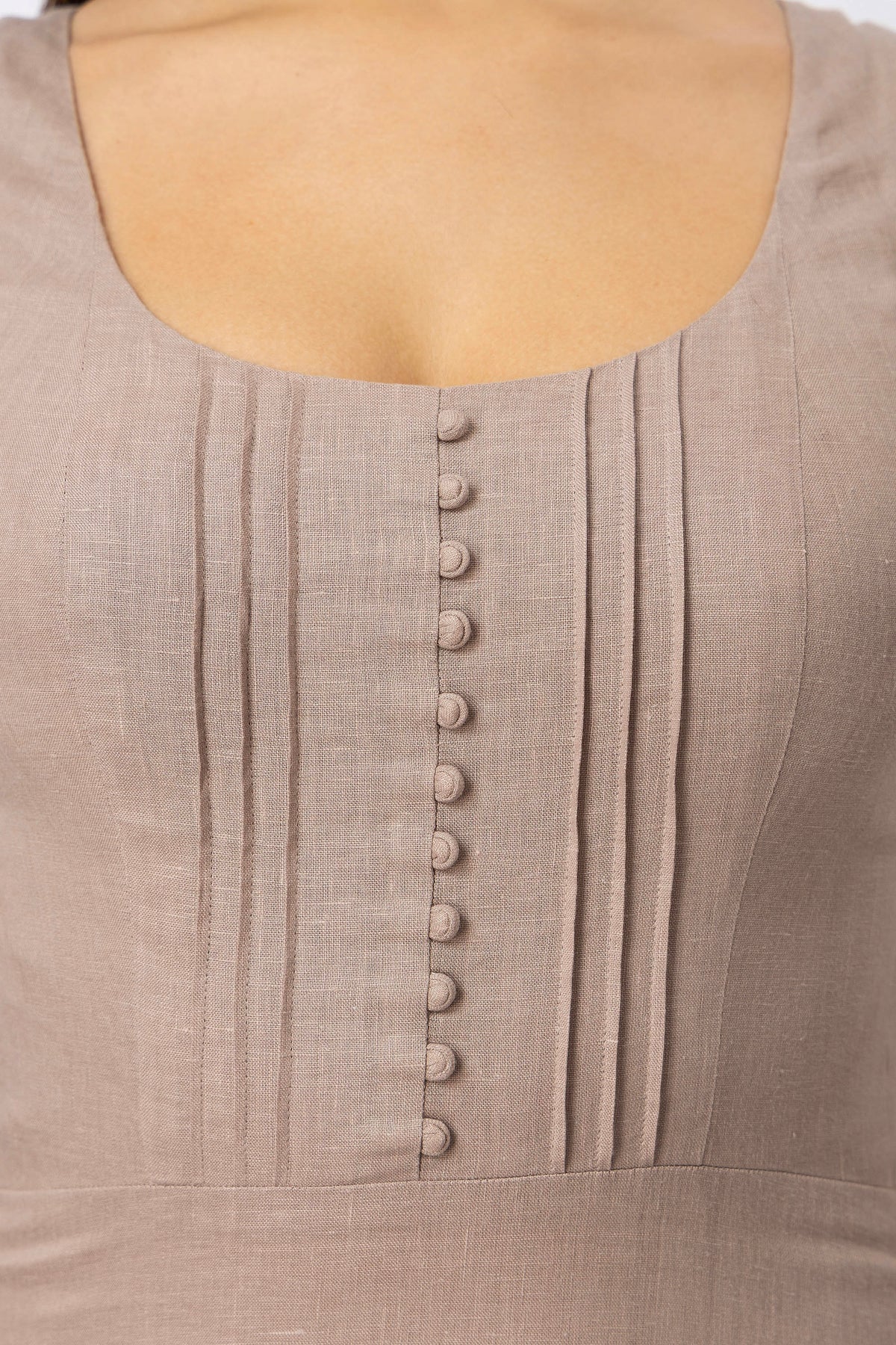 Close-up of natural linen midi dress bodice with covered buttons and pleated detailing