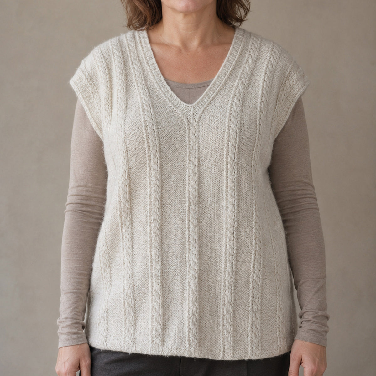 A woman wearing a cream-colored cable-knit, hand-knit, hand-spun pure pashmina cashmere sleeveless sweater vest