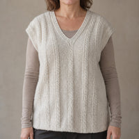 A woman wearing a cream-colored cable-knit, hand-knit, hand-spun pure pashmina cashmere sleeveless sweater vest