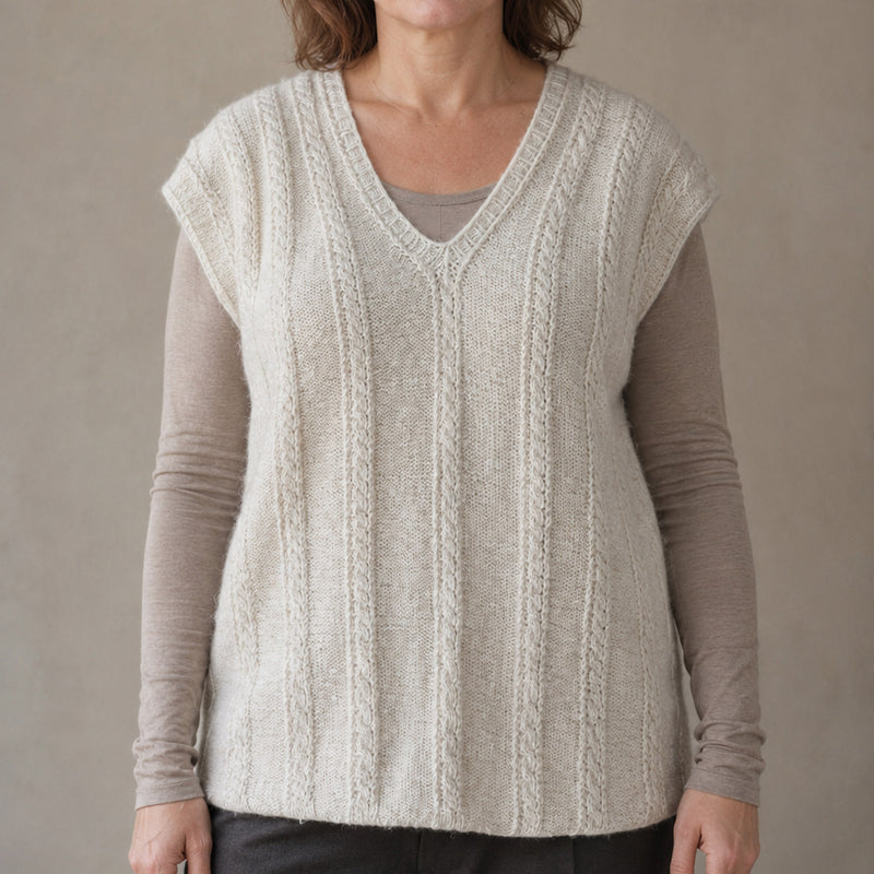 A woman wearing a cream-colored cable-knit, hand-knit, hand-spun pure pashmina cashmere sleeveless sweater vest