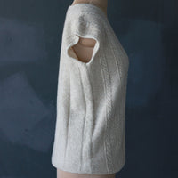 A close-up side view of a cream-colored knit cashmere sweater with a cutout shoulder detail