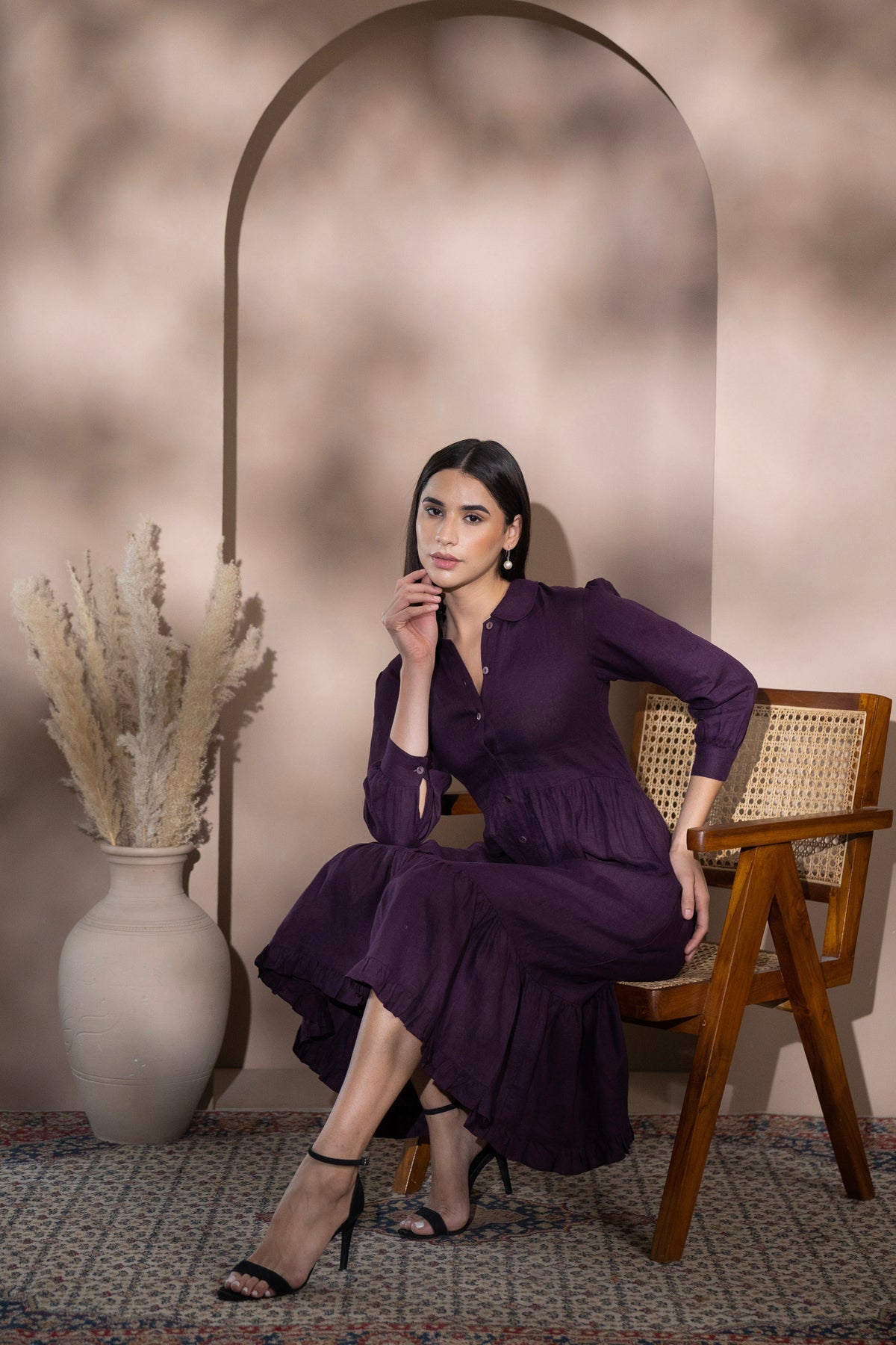 Woman wearing a linen midi dress seated on a wooden chair in an elegant interior setting