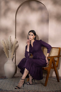Woman wearing a linen midi dress seated on a wooden chair in an elegant interior setting