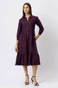 Woman wearing a long-sleeve linen shirt dress with a collared neckline, button front, gathered waist, and tiered midi skirt