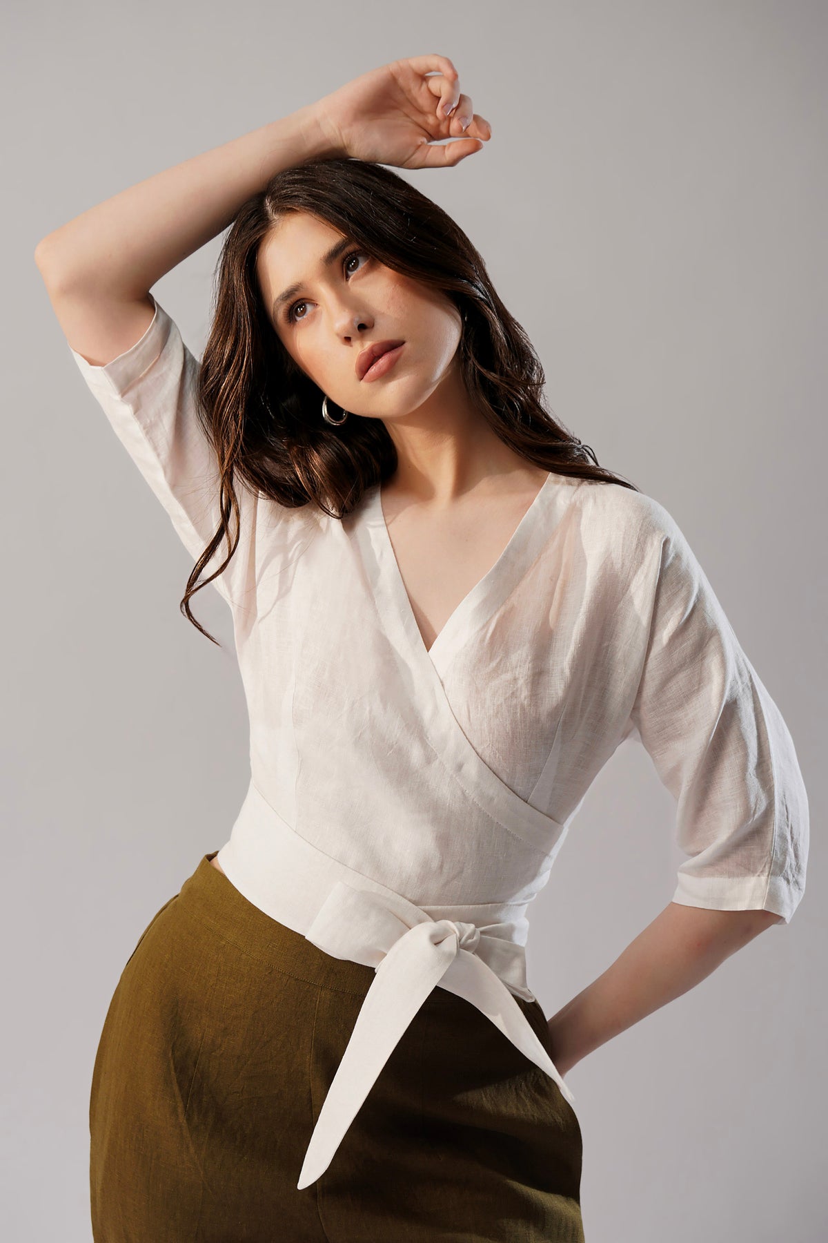 Woman wearing a white linen wrap top blouse with a tie detail and brown pant