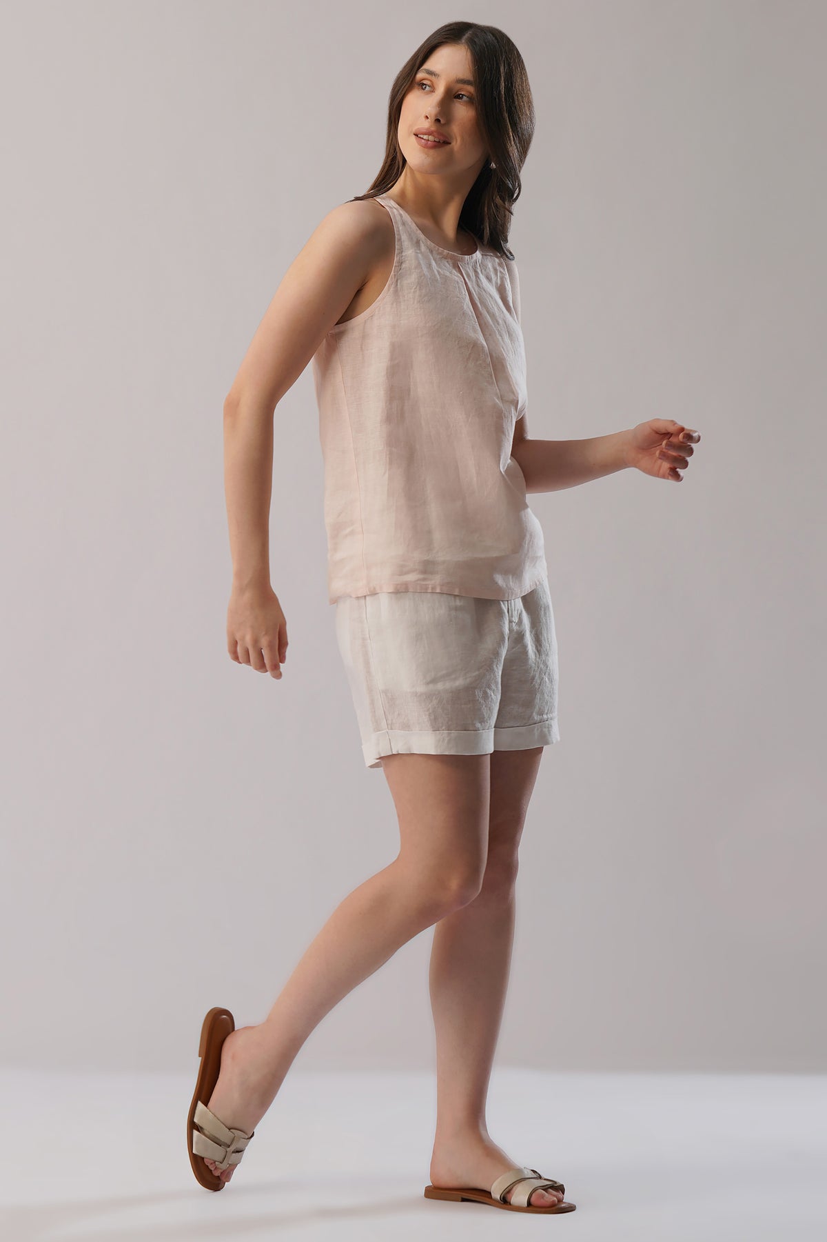 Woman wearing a soft peach sleeveless linen top and white shorts